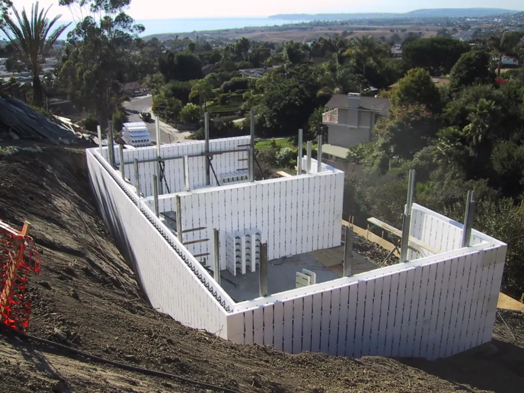 ICF basement walls stepping down a steep hillside with an ocean view beyond