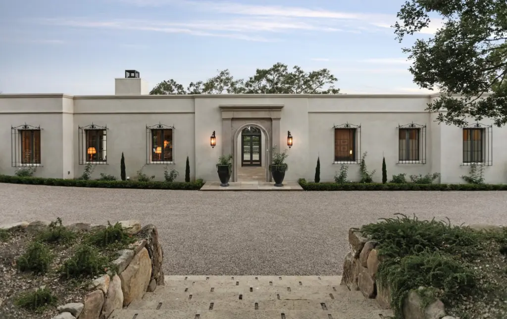 Finished light stucco single-story home with an arched entry and gravel forecourt